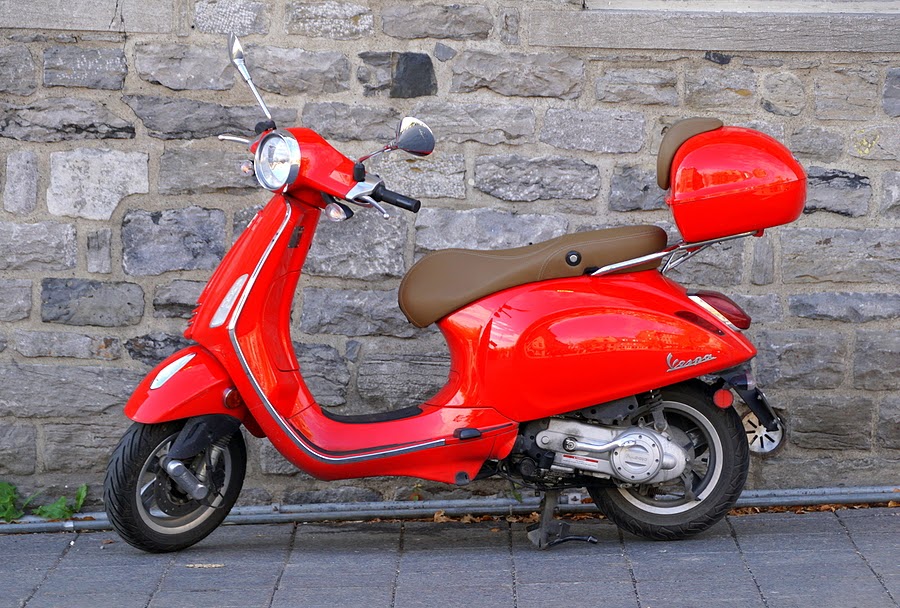 Red Vespa scooter against a brick wall
